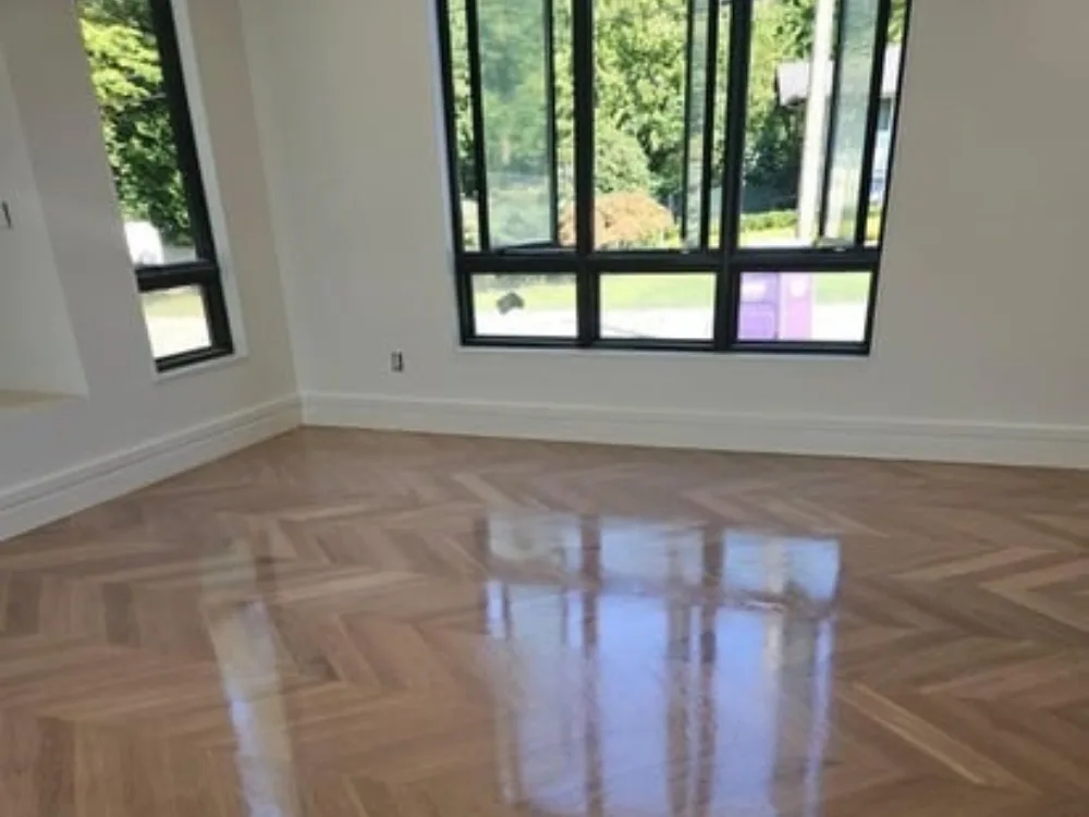 Herringbone wood floor installation in bright corner with large windows