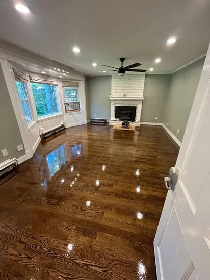Hardwood floor refinishing Sudbury featuring a high-gloss finish in a living room with a white brick fireplace.