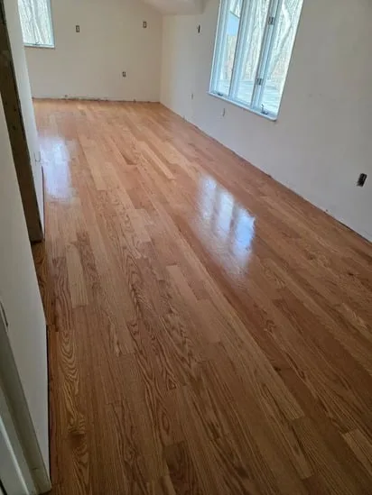 Completed hardwood floor sanding and finishing in Hebron, CT, showcasing a glossy wood surface in a large room.