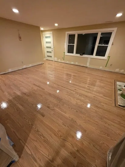 Wide perspective of a large living space featuring highly reflective, freshly completed professional hardwood floor refinishing.